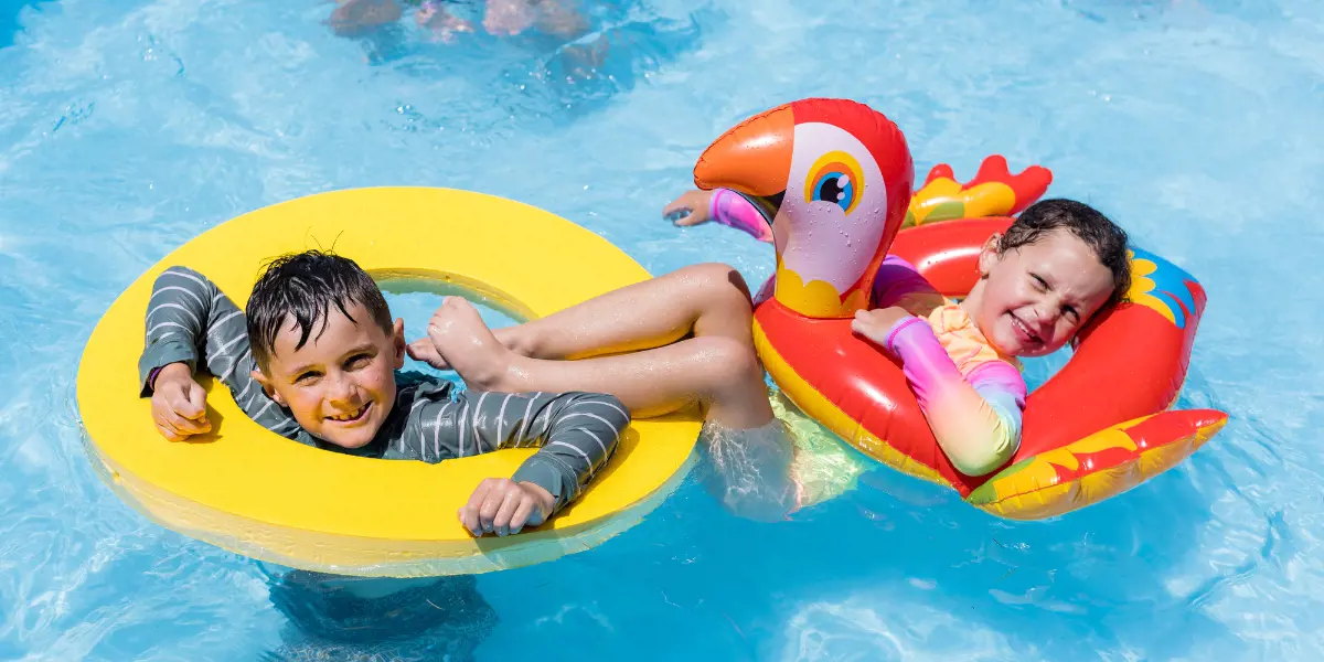 Two smiling children in brightly coloured floating rings at Waltham Summer Pool.