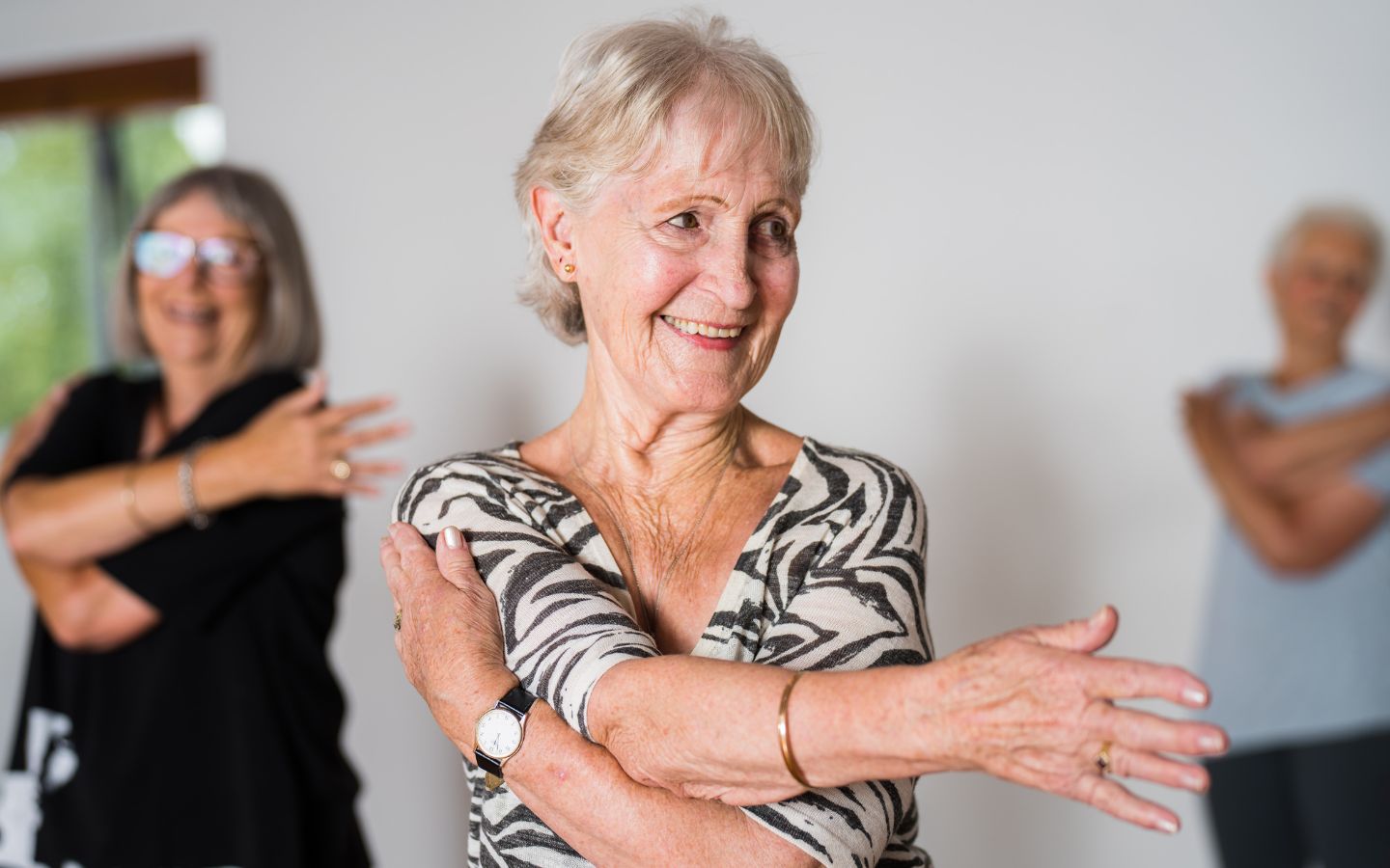 Two smiling older women stretching during a gentle exercise class at Christchurch Recreation and Sport Centre. 