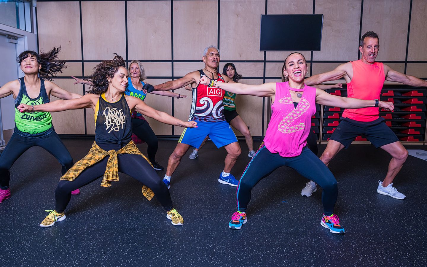 A group of smiling women and men in brightly dressed active wear dancing during a Zumba class at Christchurch Recreation and Sport.
