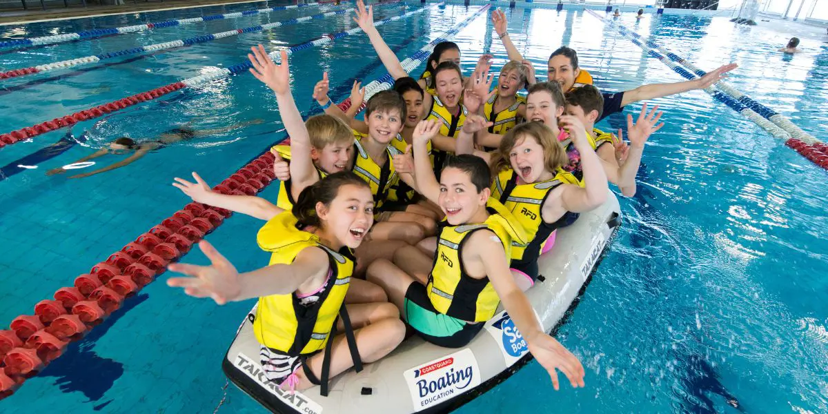 A group of children in yellow life jackets sitting in a raft at Christchurch Recreation and Sport pool.