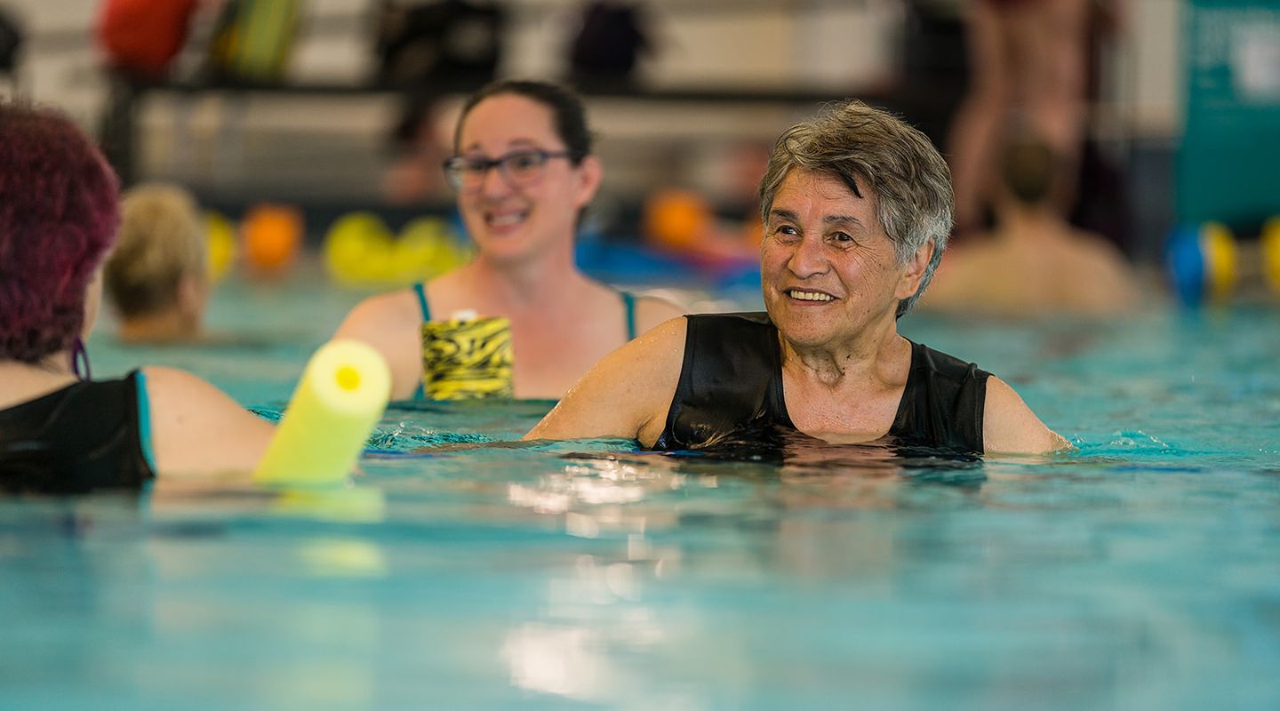 Two older women in the Matatiki Hornby pool with floatation noodles under their arms participating in an Aqua Gentle class.