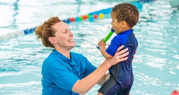 A little boy in blue swimmers jumping into the arms of a smiling swim instructor at Christchurch Recreation and Sport pool. 