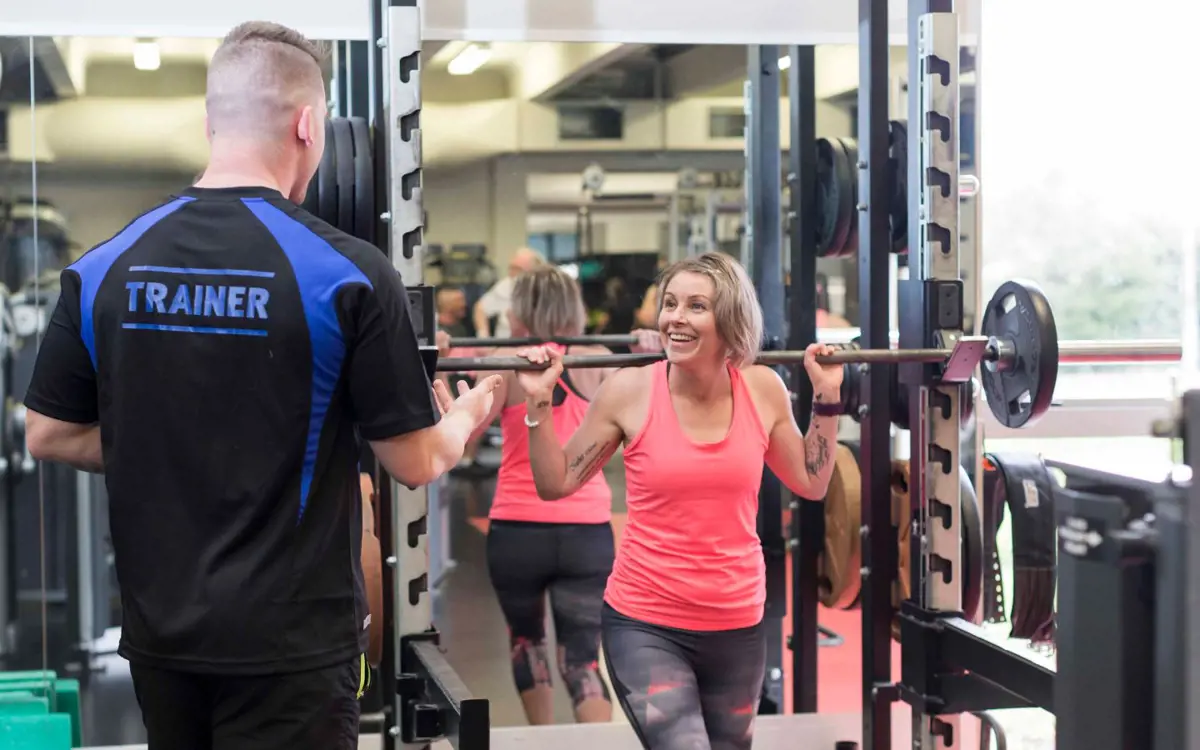 A male personal trainer assisting a woman in pink with her workout at Christchurch Recreation and Sport centre.