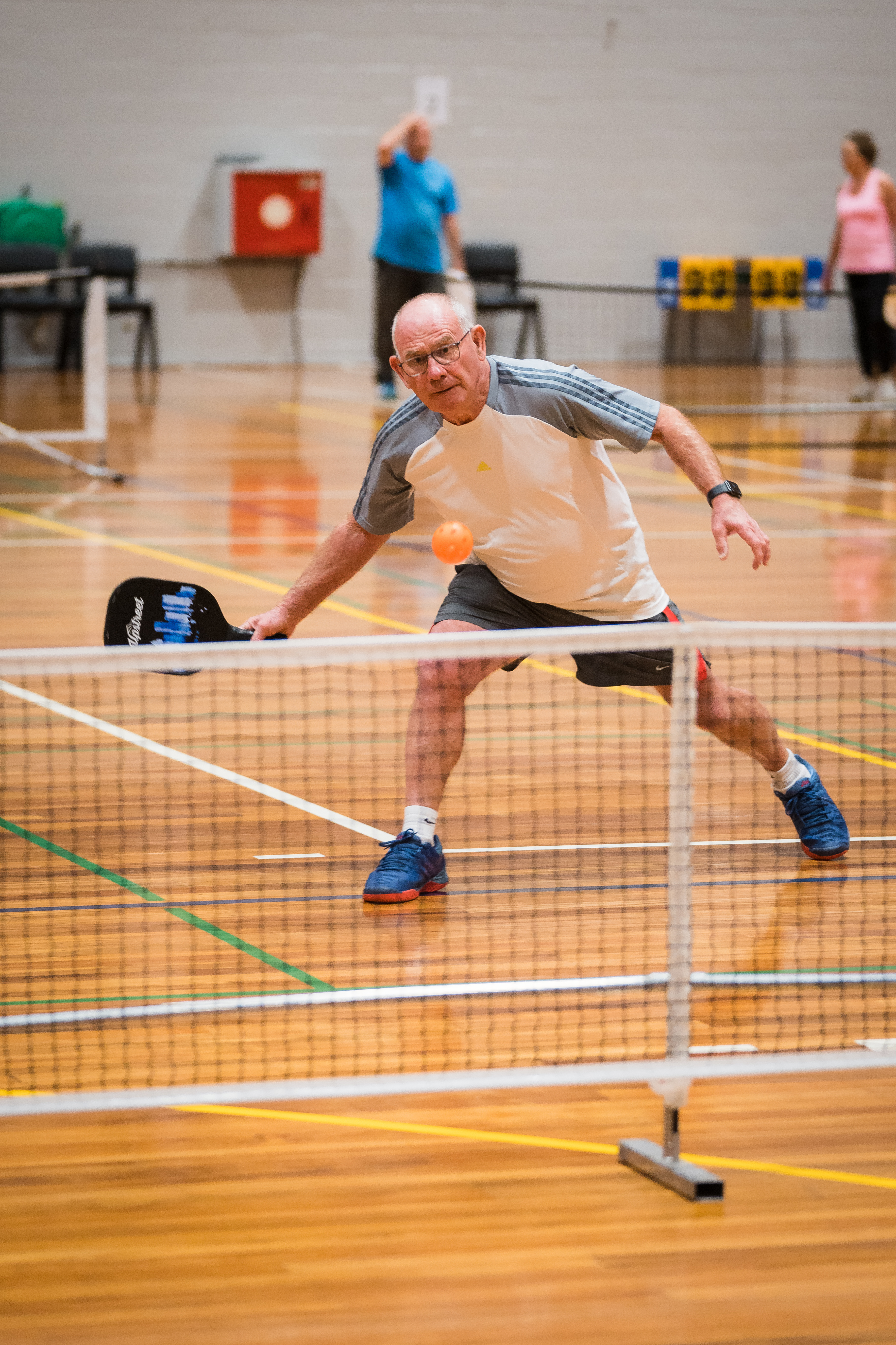 A man wearing grey hitting an orange ball while playing pickleball at Christchurch Recreation and Sport centre. 
