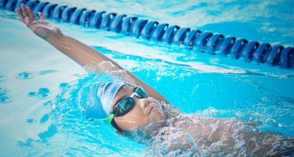 A child in a blue swim cap and goggles doing laps in the pool at Pioneer Recreation and Sport centre. 