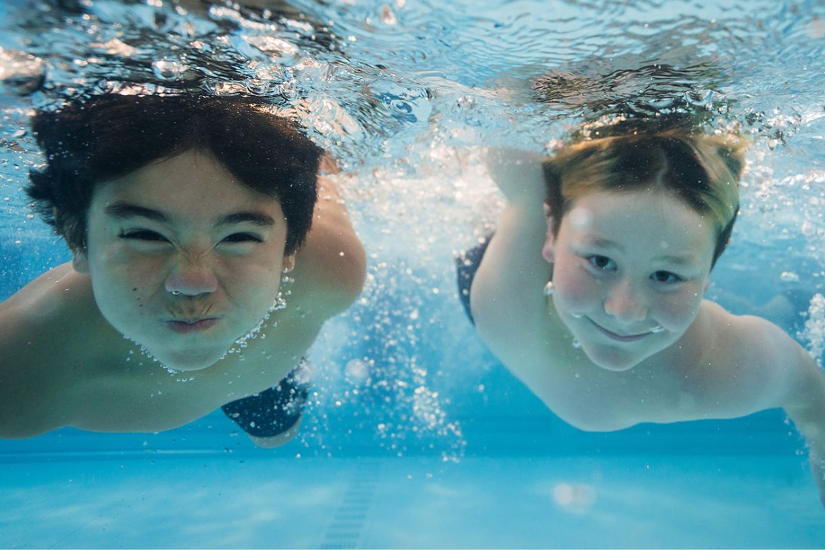 Two boys underwater with their eyes open, smiling. 