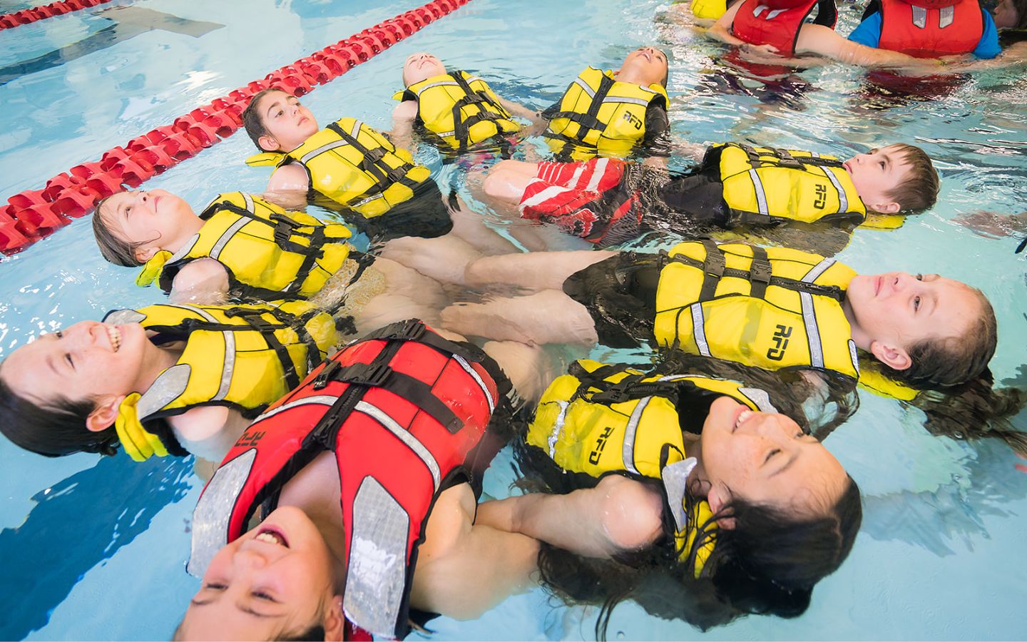 A group of children in life jackets laying on their backs in a circle at Christchurch Recreation and Sport pool. 