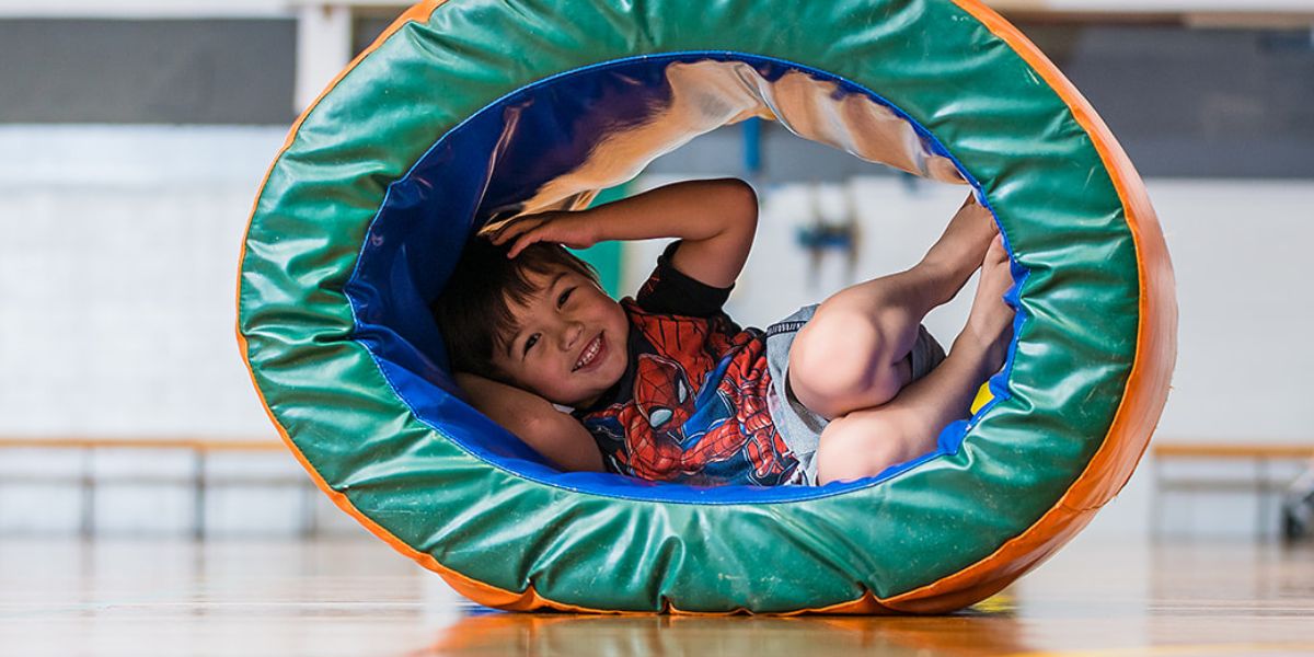 A smiling child hiding in a gymnastics ring during a tumbletimes class at Pioneer Recreation and Sport centre. 