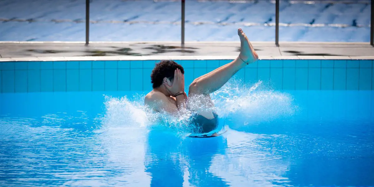 A teenage boy doing a manu off a diving board at Christchurch Recreation and Sport pool.