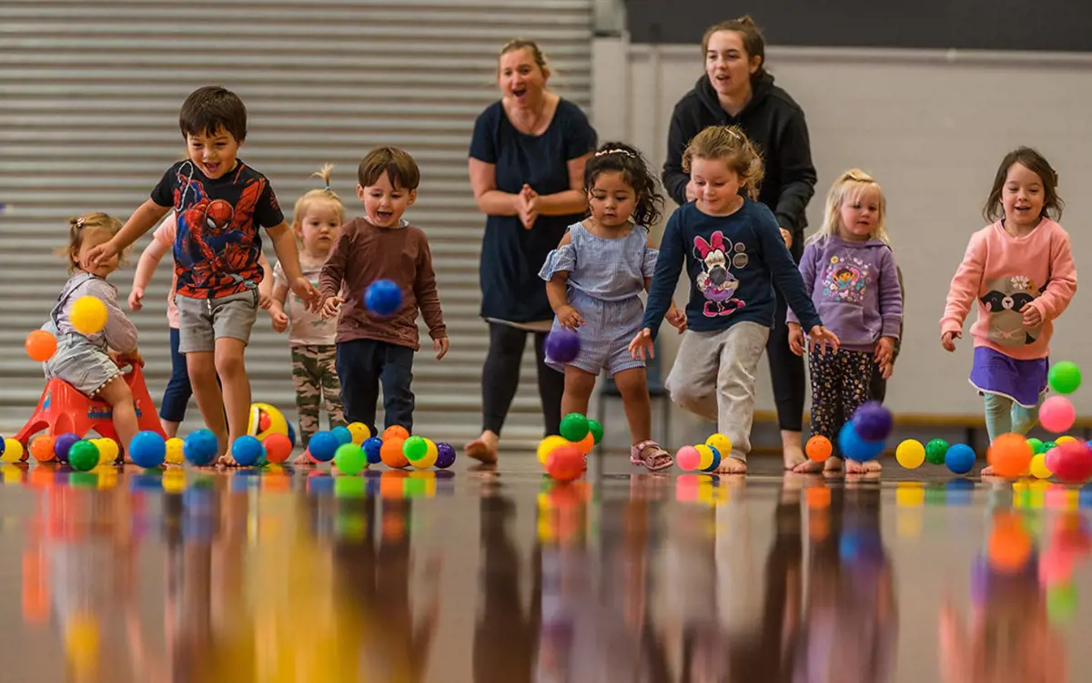 A group of toddlers running to catch multicoloured balls during a Tumbletimes class at Christchurch Recreation and Sport Centre.