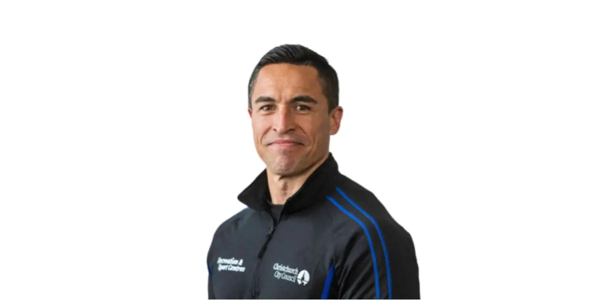 A smiling male personal trainer, Dan Hibbs, wearing a black and blue staff jacket.