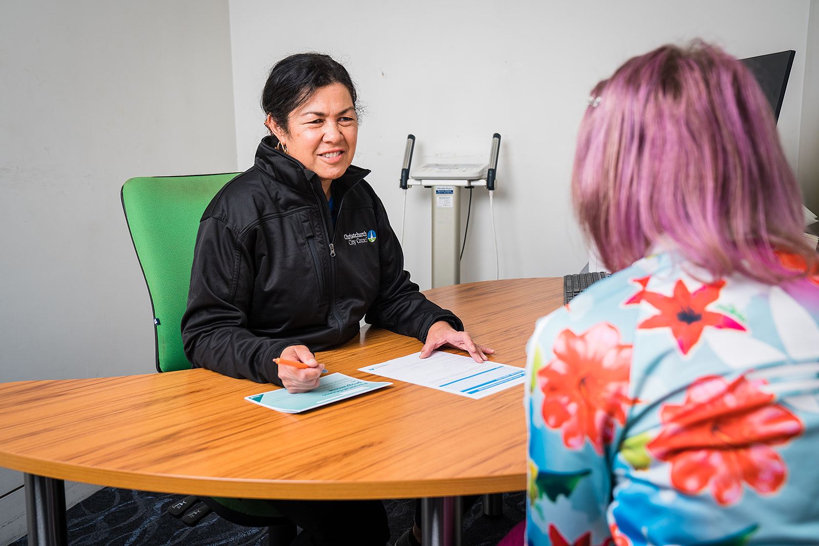 A female personal trainer in a black staff uniform sitting across a desk from a female client at Christchurch Recreation and Sport Centre.