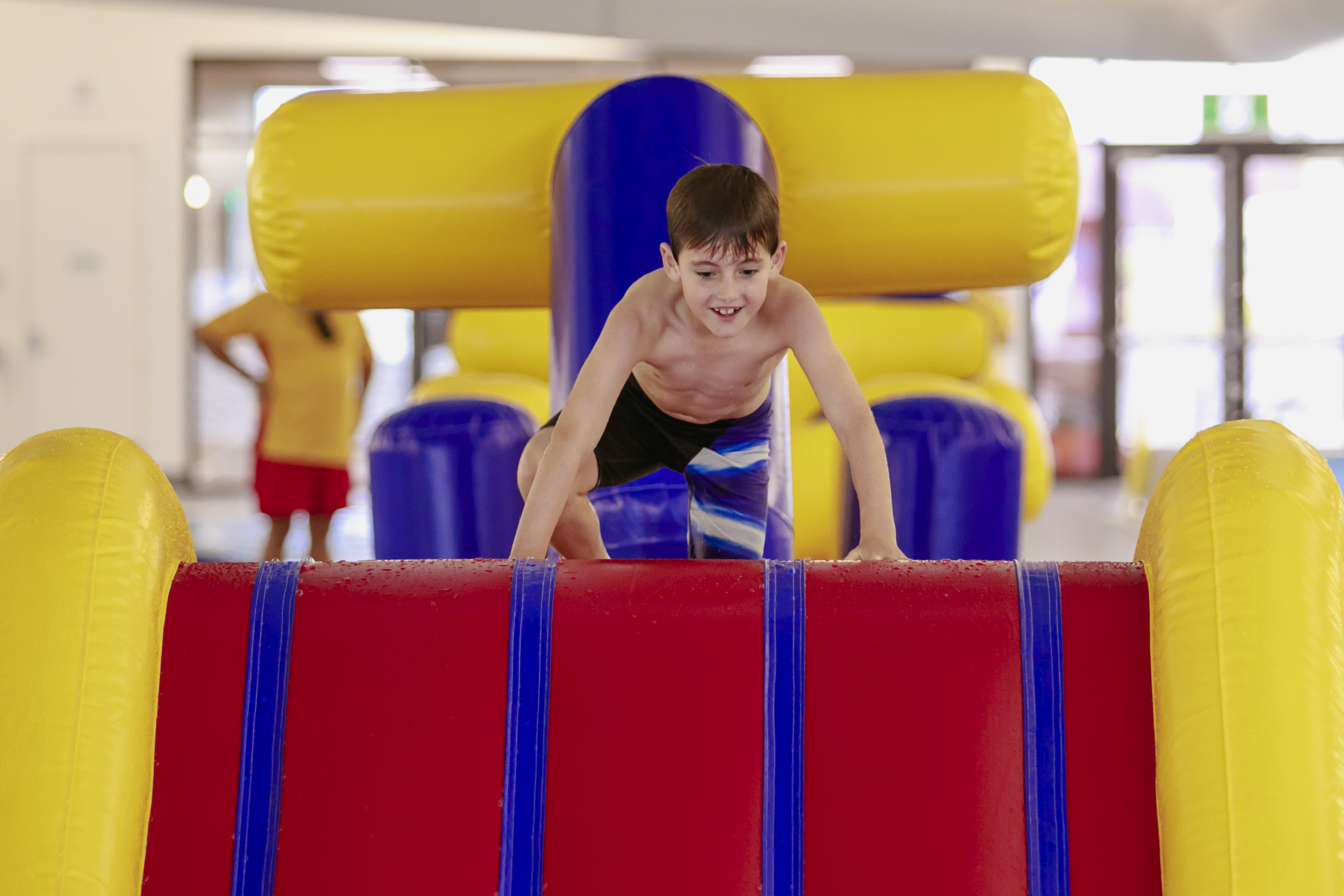 A smiling little boy climbing up to the top of the inflatable obstacle course at Mataiki Hornby pool. 