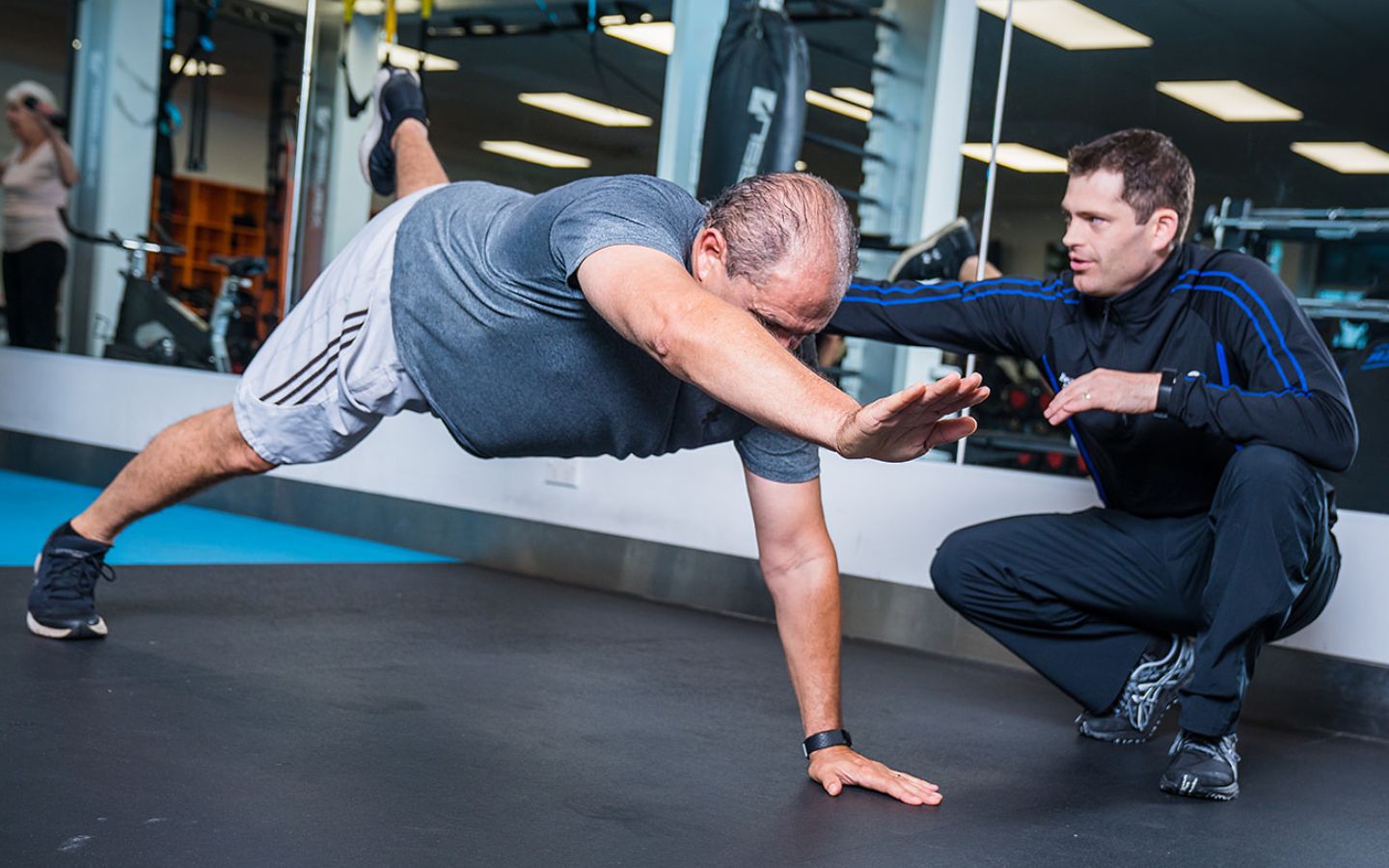 A male personal trainer guiding an older man in blue through a workout at Christchurch Recreation and Sport Centre. 
