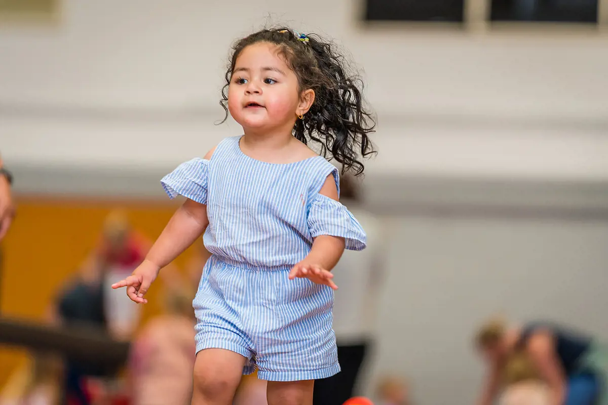 A smiling toddler running during a Tumbletimes class at Christchurch Recreation and Sport Centre.