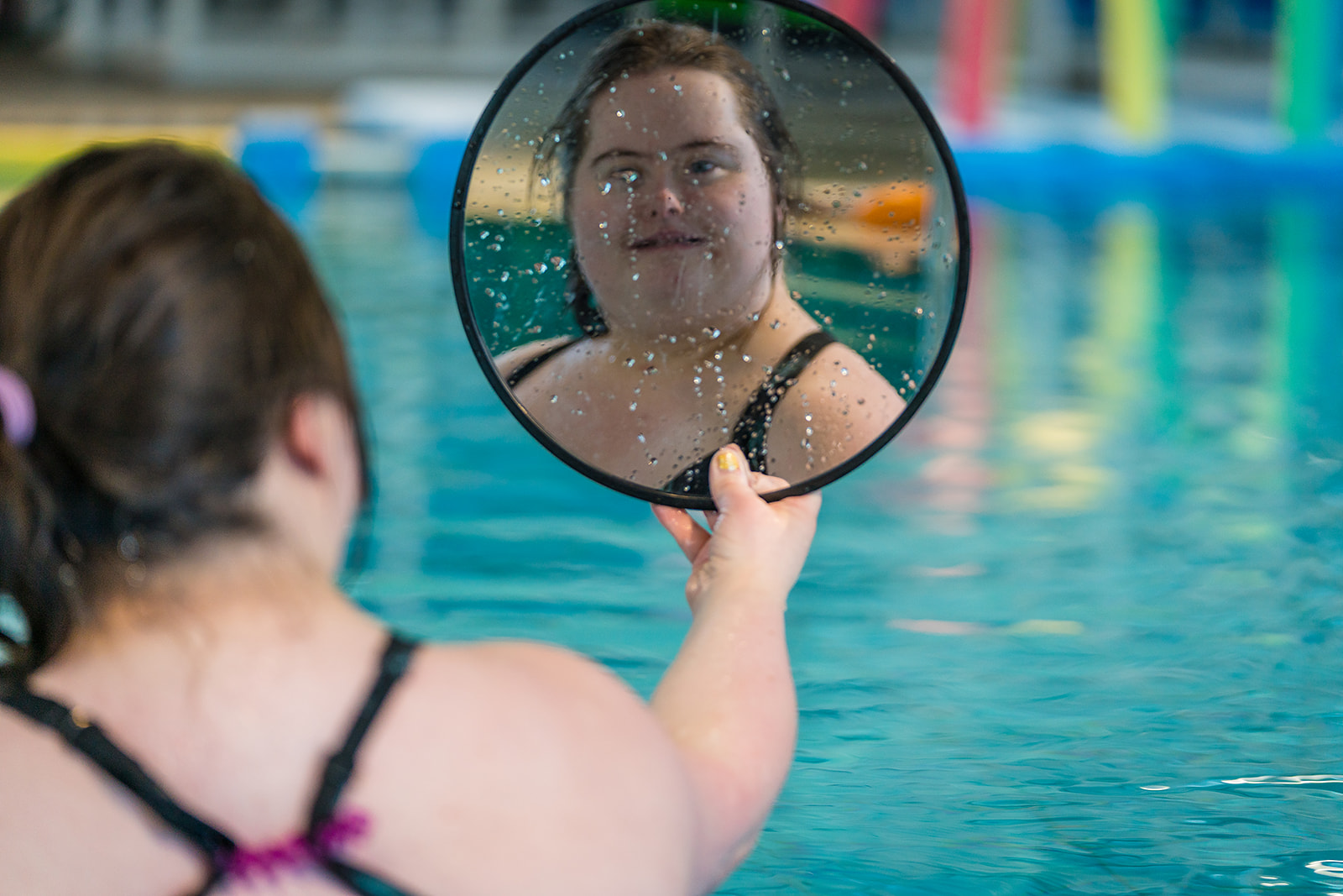 A smiling woman staring into a mirror during a Sensory Swim class at Christchurch Recreation and Sport pool. 