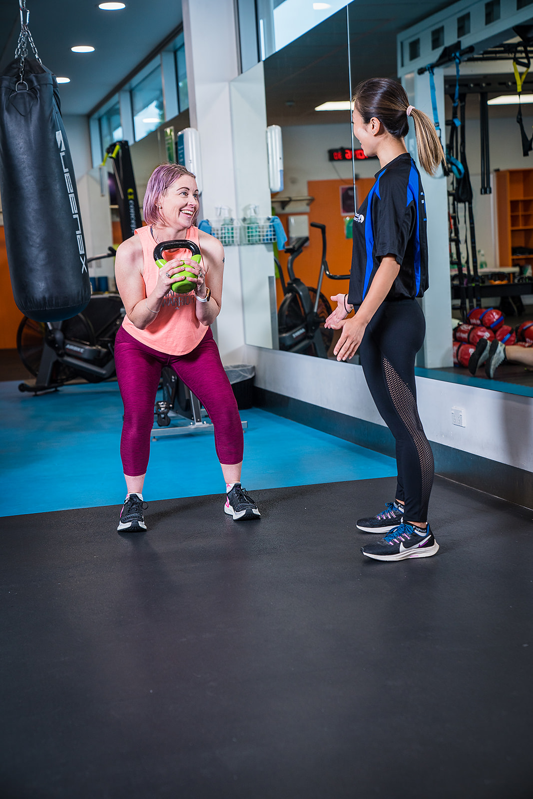 A female personal trainer assisting a woman in pink through a kettle bell workout at Christchurch Recreation and Sport Centre. 