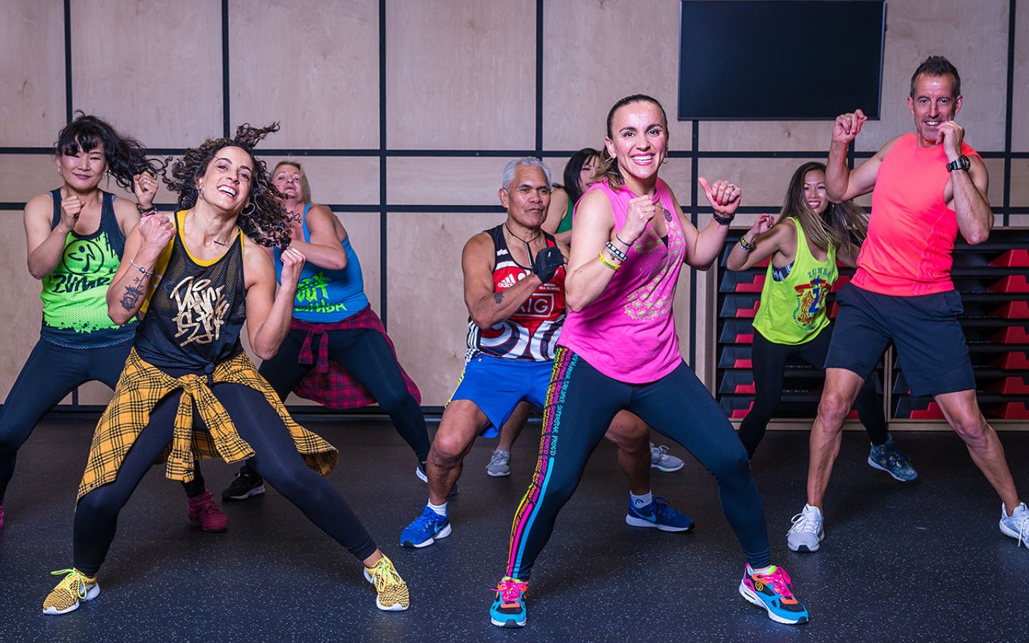 A group of smiling women and men in brightly dressed active wear dancing during a Zumba class at Christchurch Recreation and Sport.