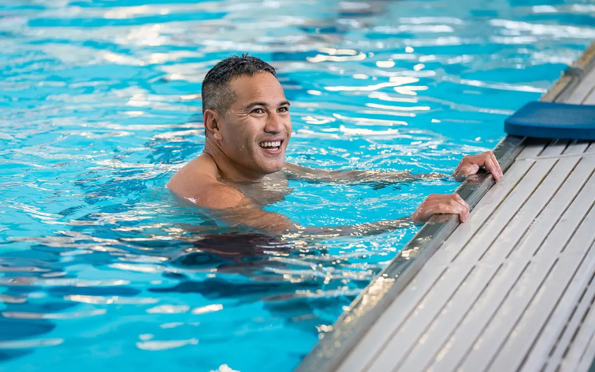 A smiling man holding onto the side of the pool at Christchurch Recreation and Sport pool.