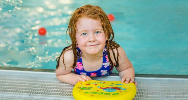 A smiling little girl holding onto a flotation board while attending a Frogs class at Christchurch Recreation and Sport pool. 