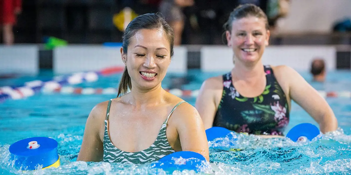 Two women participating in an Aqua Zumba class while holding floatation dumbbell weights A group of eight adults participating in an Aqua Zumba class while holding floatation dumbbell weights at A group of eight adults participating in an Aqua Zumba class at Christchurch Recreation and Sport pool.