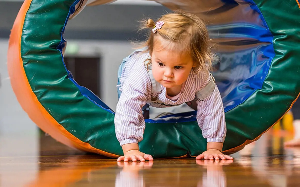 A smiling toddler hiding inside a foam ring during a Tumbletimes class at Christchurch Recreation and Sport Centre.
