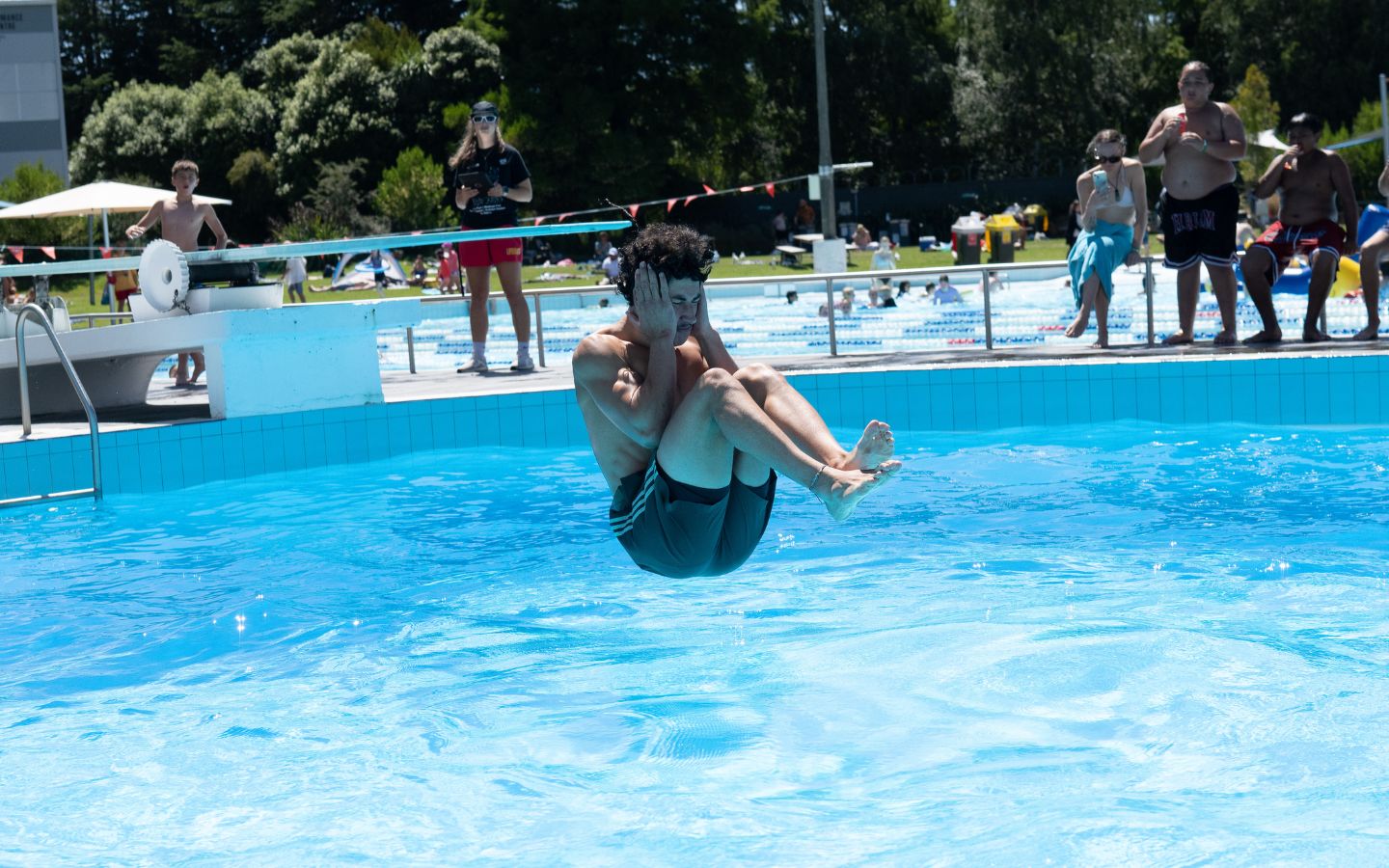 A teenage boy doing a manu off a diving board at Christchurch Recreation and Sport summer pool. 