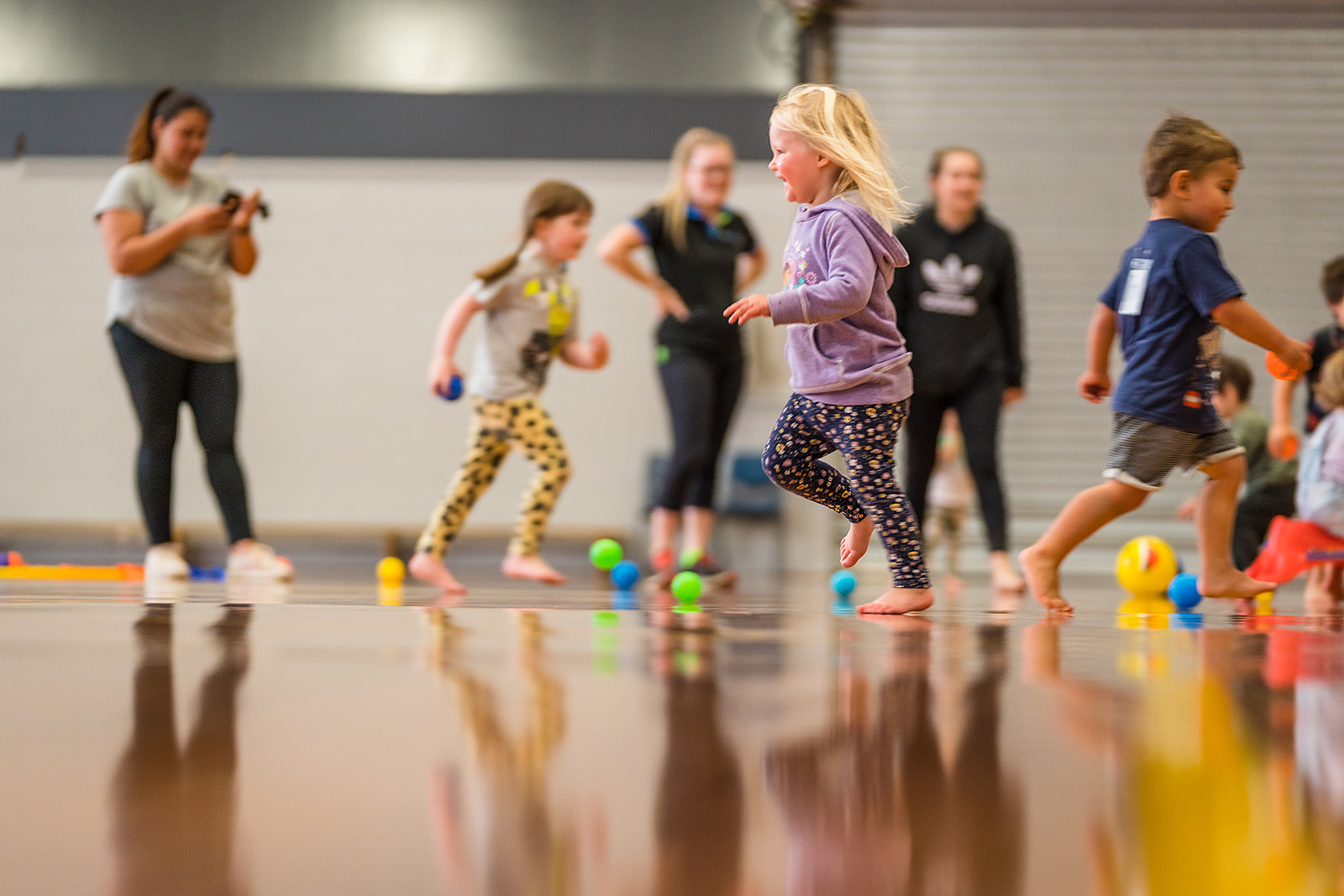 Children running to pickup brightly coloured balls during a Pre-school sports class at Graham Condon Recreation and Sport Centre. 