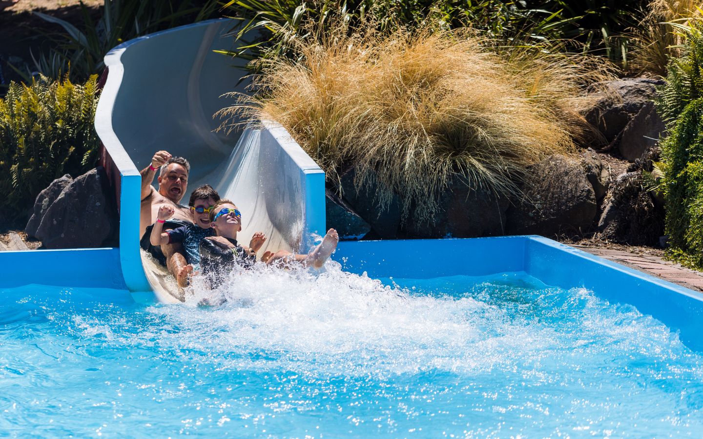 Two smiling boys and a man sliding down the Halswell Summer Pool hydroslide. 