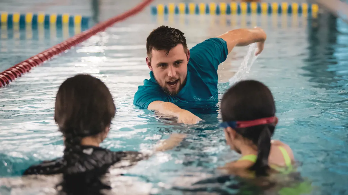 A male swim instructor demonstrating front stroke to two children at Christchurch Recreation and Sport.