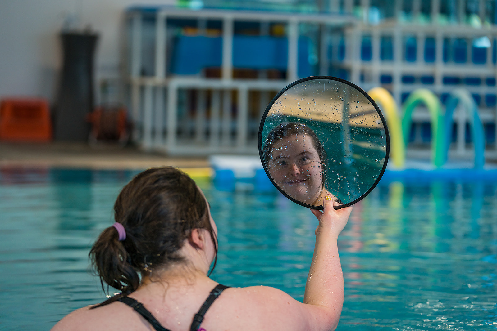 A smiling woman staring into a mirror during a Sensory Swim class at Christchurch Recreation and Sport pool. 