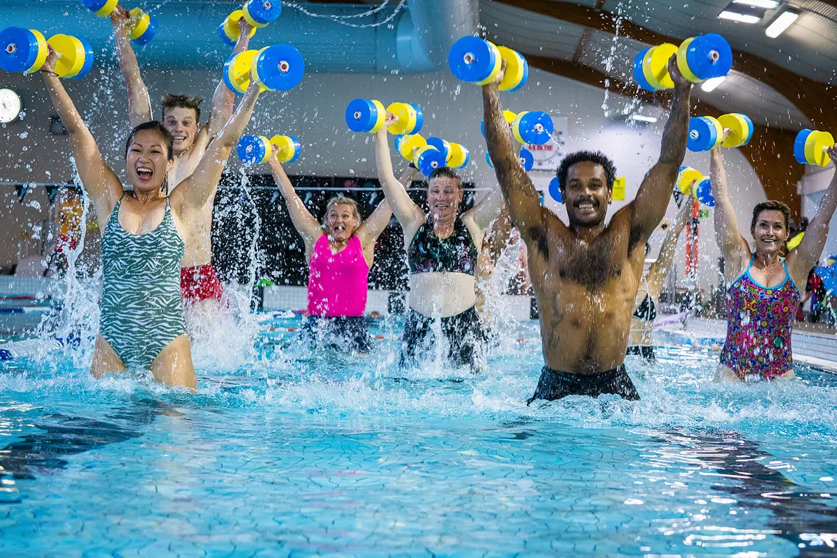 A group of eight adults participating in an Aqua Zumba class while holding floatation dumbbell weights at A group of eight adults participating in an Aqua Zumba class at Christchurch Recreation and Sport pool.